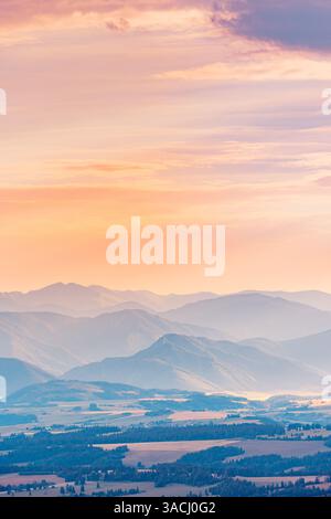 Lichtschichten bei Sonnenuntergang über Bergen, atemberaubende, warme Farbtöne, die Schatten werfen und eine ruhige, farbenfrohe Landschaft in der Dämmerung, nebeliger Natur schaffen Stockfoto