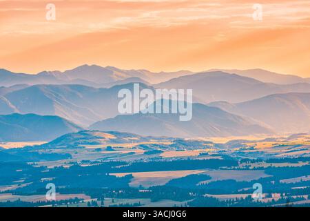 Lichtschichten bei Sonnenuntergang über Bergen, atemberaubende, warme Farbtöne, die Schatten werfen und eine ruhige, farbenfrohe Landschaft in der Dämmerung, nebeliger Natur schaffen Stockfoto
