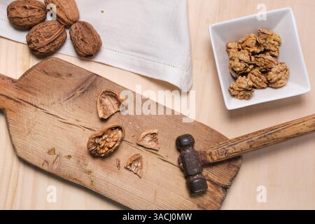 Zenithal-Ebene eines zerrissenen Nussstücks und Hammer auf Holzpaddel mit geschälten Nüssen in der Schüssel Stockfoto