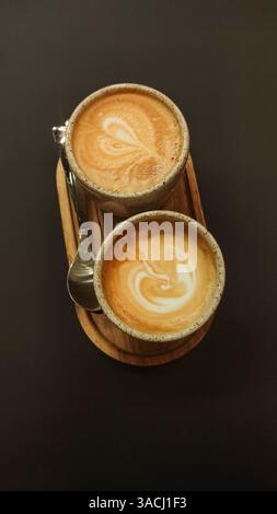 Zwei Tassen Cappuccino, dekoriert mit Latte Art Herzen, sitzen auf einem Holztablett und schaffen eine gemütliche und einladende Szene, die perfekt zum Teilen ist Stockfoto