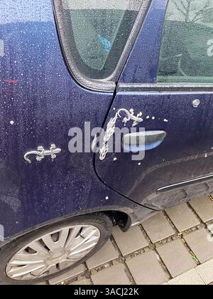 Crema, Italien - 2. März 2025 Regentropfen glitzern auf einem dunkelblauen Mitsubishi Carisma, mit auffälligen Metallic-Geckos und Flammenaufklebern, geparktem Gra Stockfoto