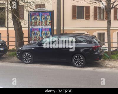 Crema, Italien - 2. März 2025 auf einer Straße in Cremona, Italien, befindet sich ein schwarzer Fiat Tipo Station Wagon neben lebendigen Plakaten, die eine bevorstehende Werbung anzeigen Stockfoto