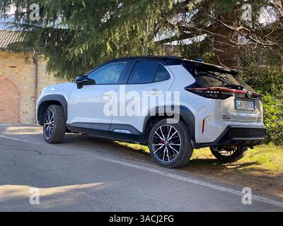 Crema, Italien - 2. März 2025 moderner weißer Toyota Yaris Cross Hybrid-Wagen, der in der Nähe eines historischen Gebäudes mit Steinmauern geparkt ist und sein elegantes Design unterstreicht Stockfoto