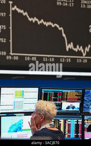 04. April 2025, Hessen, Frankfurt/Main: Eine Traderin beobachtet ihre Monitore auf dem Börsenboden der Frankfurter Wertpapierbörse, während die Anzeigetafel mit der Dax-Kurve fallende Preise anzeigt. US-Präsident Donald Trump hatte ein riesiges Zollpaket gegen Handelspartner auf der ganzen Welt veröffentlicht, und das chinesische Finanzministerium hat Gegenzölle auf US-Importe in Höhe von 34 % angekündigt, die am 10. April in Kraft treten sollen. Foto: Arne Dedert/dpa Stockfoto