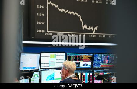 04. April 2025, Hessen, Frankfurt/Main: Eine Börsenhändlerin beobachtet ihre Monitore auf dem Handelsplatz der Frankfurter Wertpapierbörse, während die Anzeigetafel mit der Dax-Kurve fallende Preise anzeigt. US-Präsident Donald Trump hatte ein riesiges Zollpaket gegen Handelspartner auf der ganzen Welt veröffentlicht. Das chinesische Finanzministerium hat Gegenzölle auf US-Importe in Höhe von 34 % angekündigt, die am 10. April in Kraft treten sollen. Foto: Arne Dedert/dpa Stockfoto