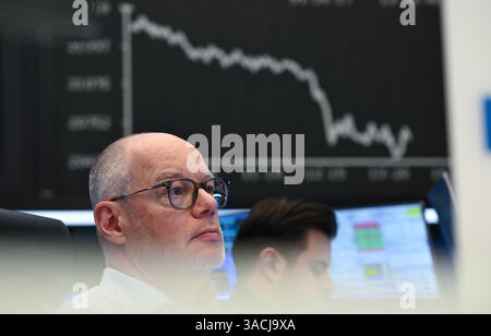 04 April 2025, Hessen, Frankfurt/Main: Börsenhändler beobachten ihre Monitore auf dem Börsenboden der Frankfurter Wertpapierbörse, während die Anzeigetafel mit der Dax-Kurve fallende Preise anzeigt. US-Präsident Trump hatte ein riesiges Zollpaket gegen Handelspartner auf der ganzen Welt veröffentlicht. Die Europäische Union und China haben bereits Gegenmaßnahmen angekündigt. Foto: Arne Dedert/dpa Stockfoto