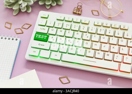 Online-Test. Computertastatur mit Wort auf grünem Knopf und Schreibwaren auf rosa Tisch Stockfoto