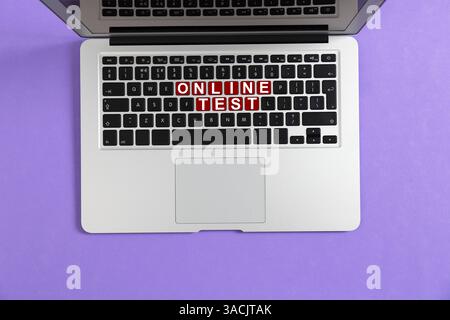 Online-Test. Laptop-Tastatur mit Tasten, die Wörter auf violettem Hintergrund erzeugen, Ansicht von oben Stockfoto