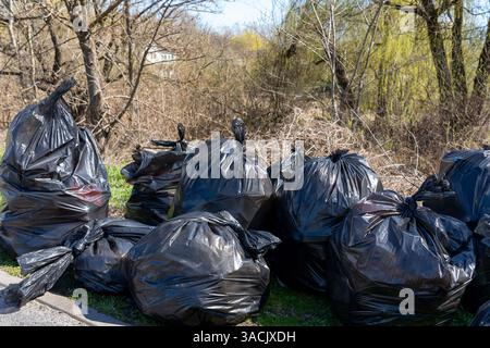 Schwarze Müllsäcke stapeln sich entlang einer Straße, umgeben von kargen Bäumen und Bürsten. Die Einstellung scheint ein Bereich im frühen Frühjahr zu sein, mit Zeichen o Stockfoto
