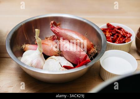 Eine Metallschale mit frischem Knoblauch, Schalotten und roter Chili, umgeben von Zucker und getrockneten Chilis in kleinen Behältern. Stockfoto