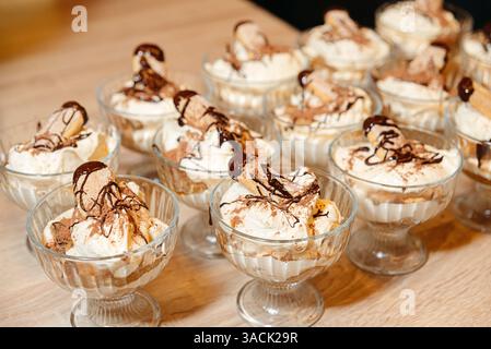 Individuelle Desserttassen im Tiramisu-Stil mit Schlagsahne, Kakaopulver, Marienfinger und geschmolzener Schokoladensauce. Stockfoto