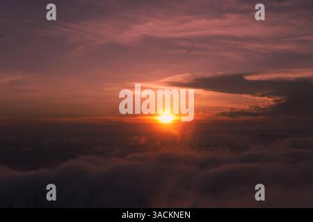 Der goldene Sonnenaufgang erleuchtet den Himmel mit sanften violetten und orangen Tönen über einer Wolkendecke, die eine friedliche und traumhafte Aussicht vom Gipfel des Berges bietet. Stockfoto