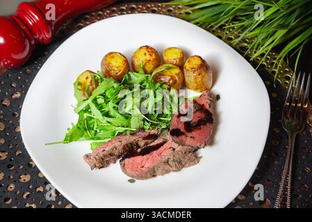 Ein Gourmet-Teller mit geschnittenem gegrilltem Rindersteak mit Balsamico-Glasur, gebratenen Babykartoffeln und frischem Rucola auf einem weißen Gericht. Stockfoto