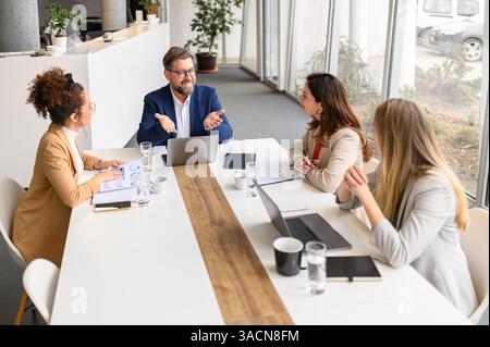 Hochwinkelansicht eines männlichen Anwalts mit Gesten auf dem Laptop und Erläuterung von Projektdetails für weibliche Kollegen im Meeting Stockfoto