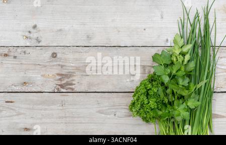 Ein Haufen frischer Petersilie, Schnittlauch und Frühlingszwiebeln auf hellem hölzernem Hintergrund, Stockfoto