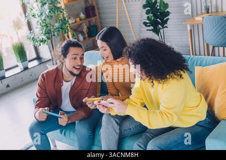 Junge Freunde, die gemeinsam eine lustige Gaming-Session in einem gemütlichen und stilvollen Wohnzimmer mit fröhlicher Atmosphäre genießen. Stockfoto