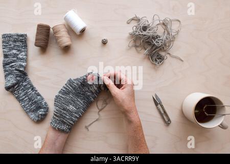 Frauenhände reparieren ein Loch in einer Socke Stockfoto