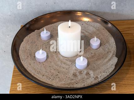 Elektrische LED-Kerzen in Sand in einer großen Schüssel. Innenraum. Stockfoto