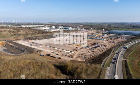 Luftaufnahme einer großen Baustelle mit Erdbewegungsmaschinen, einer Autobahn, Windturbinen und einem großen Industrielager im Hintergrund Stockfoto