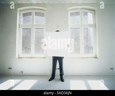 Mann, der im Zimmer steht und den Plan des Architekten vor Augen hält Stockfoto