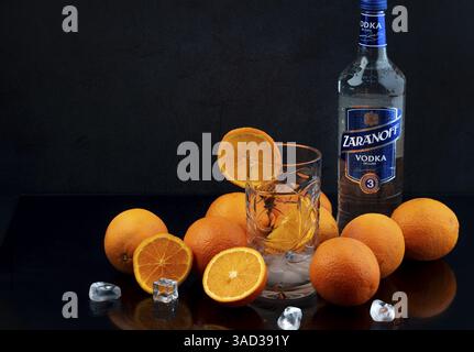 Wodkaflasche mit frischen Orangen, Eiswürfeln und einem Glas auf dunklem Hintergrund, Studioaufnahme Stockfoto