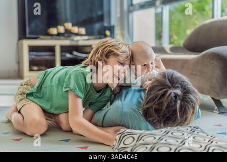 Vater, Sohn und neugeborenes Baby liegen auf dem Boden in einem gemütlichen Kinderzimmer und feiern die Ankunft ihres neuesten Familienmitglieds. Elternschaft, Bindung und Stockfoto
