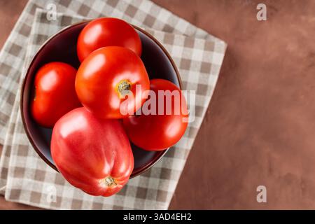 Frische rote Tomaten in Schüssel auf karierter Serviette, Kopierraum Stockfoto