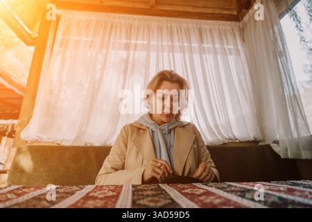 Eine Frau in einem beigen Mantel schaut sich ein kleines schwarzes Objekt an Stockfoto
