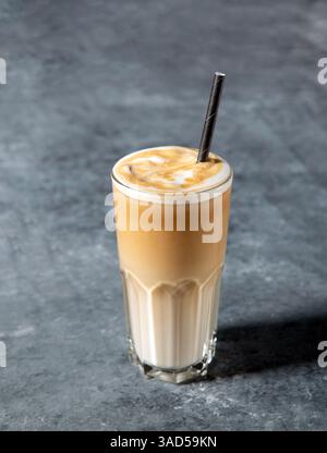 Eiskaffee Latte in einem hohen Glas mit Creme oder Milch und Strohhalm auf grauem Hintergrund mit Kopierraum Stockfoto