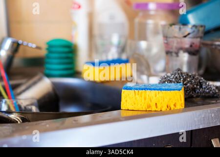 In einem durchschnittlichen Spülbecken gibt es einen gelben und blauen Schwamm, der geduldig dort liegt und bereit ist, den Reinigungsprozess zu unterstützen Stockfoto