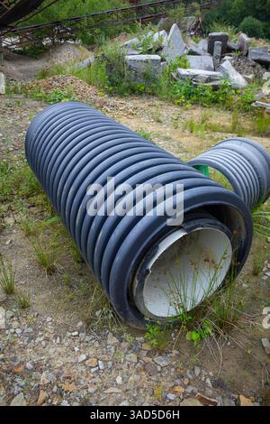 Ein Rohr liegt auf dem Boden neben einem Steinhaufen. Das Rohr ist schwarz-weiß und von Gras umgeben Stockfoto