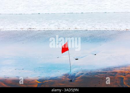 Die heutigen Strandbedingungen erfordern Vorsicht, wie durch die rote Flagge angezeigt. Der Strand mit roter Flagge ist deutlich im Sand gepflanzt und dient als klare Warnung Stockfoto