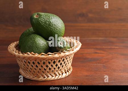 Ganze Avocados in Korb auf Holztisch, Großaufnahme. Leerzeichen für Text Stockfoto