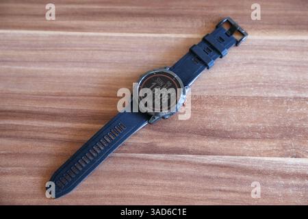 Eine robuste Smartwatch mit einer digitalen Anzeige, die Uhrzeit, Datum, Schritte und Herzfrequenz anzeigt, auf einer Holzoberfläche platziert. Stockfoto