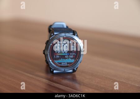 Eine robuste Smartwatch mit einer digitalen Anzeige, die Uhrzeit, Datum, Schritte und Herzfrequenz anzeigt, auf einer Holzoberfläche platziert. Stockfoto