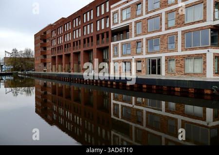 Moderne Backsteingebäude säumen den Kanal bei Punt Sniep in Diemen. Ihre markante Symmetrie und ruhigen Reflexionen verbinden urbane Architektur mit Ruhe Stockfoto