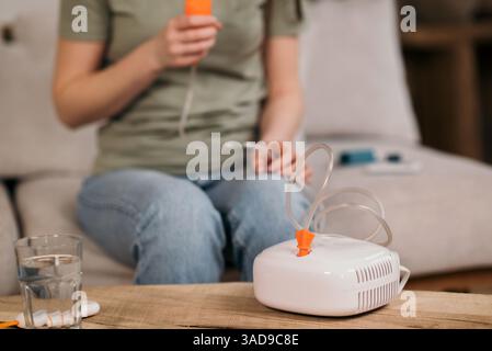 Frau, die zu Hause einen Vernebler zur Atembehandlung verwendet, auf einer Couch sitzt und medizinische Geräte auf dem Tisch hat. Stockfoto