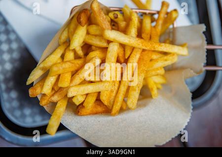 Aus nächster Nähe sehen Sie goldene, knusprige Pommes frites, die in einem stilvollen Korb mit braunem Pergamentpapier serviert werden. Ideal zum Fotografieren von Speisen und Restaurants Stockfoto