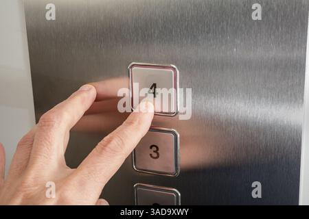 Person, die die Fahrstuhltaste drückt. Weibliche Passagierin auf Ebene 4. Nahaufnahme einer Frau, die einen Knopf mit einer Edelstahl-Gegensprechanlage drückt. . Selektiv fo Stockfoto