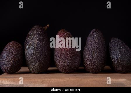 HASS Avocado auf Holztisch. Die Hass Avocado ist eine Vielzahl von Avocado mit dunkelgrüner, holpriger Haut. Stockfoto