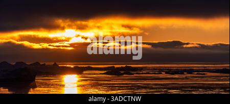 Ein atemberaubender Sonnenuntergang über einem ruhigen Meer, mit goldenen und orangen Tönen, die sich vom Wasser reflektieren. Eisberge sind im Vordergrund sichtbar und erzeugen ein heiteres A Stockfoto