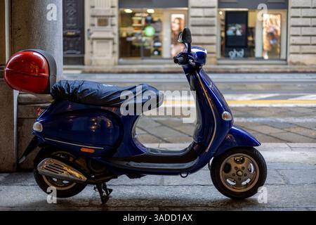 Turin, Italien - 10. November 2021: Ein blauer Vespa LX 150 Roller mit rotem Topcase parkt auf einem Bürgersteig in der Nähe von Geschäften Stockfoto