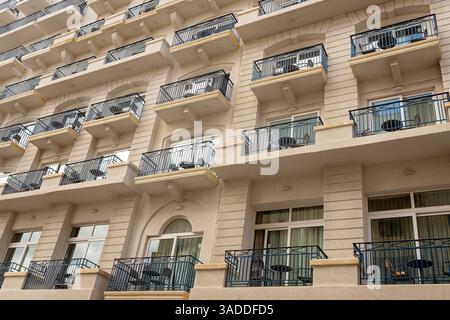 Die Fassade des wunderschönen mehrstöckigen Gebäudes mit einheitlichen schwarzen Metallbalkonen, großen Fenstern und beigefarbenen Steinmauern Stockfoto