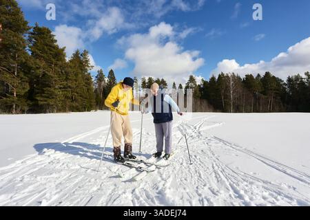 Reifer Mann räumt Schnee von seinen Skiern, während er während eines Familienskiausflugs über die Skier seiner Frau fährt. Stockfoto