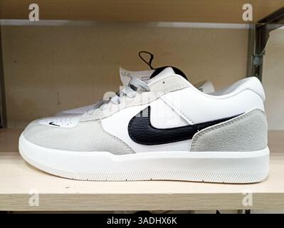Aktau, Kasachstan - 22. März 2025: Weiß-grauer Sneaker mit schwarzem Swoosh auf Holzregal. Stockfoto