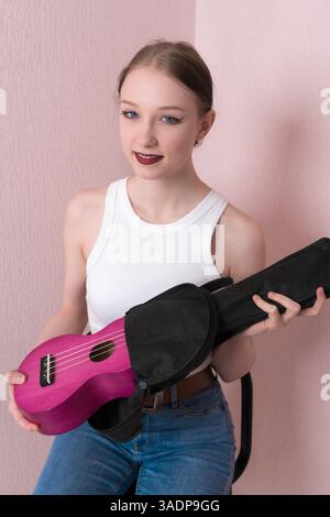 Die junge Musikerin nimmt Musikinstrumente-Ukulele aus der schwarzen Tasche und schaut in die Kamera. Freundliche 18-jährige kaukasische Musikerin Stockfoto