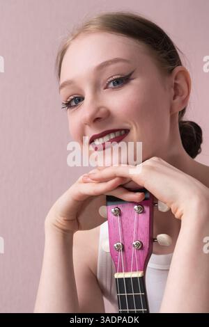 Porträt einer jungen Frau mit Ukulele in der Kamera. Junge Musikerin mit aufrichtigem Lächeln, positivem Auftreten, freundlichem Ausdruck. Sie ist der Kopf Stockfoto