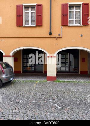 San Secondo Parmense, Italien 1. März 2025 verwittertes orangenes Gebäude mit leuchtenden roten Fensterläden und dekorativen Bögen, die den traditionellen Archit hervorheben Stockfoto