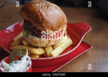 Köstlicher Hamburger mit Pommes frites, serviert auf einem lebhaften roten Teller Stockfoto