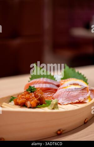 Sashimi-Set mit Lachs, serviert auf einem hölzernen Sushi-Boot, mit Zitrone und Wasabi Stockfoto